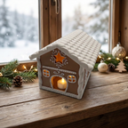 Lebkuchenhaus mit warm leuchtendem LED-Teelicht auf einer weihnachtlichen Chalet-Fensterbank